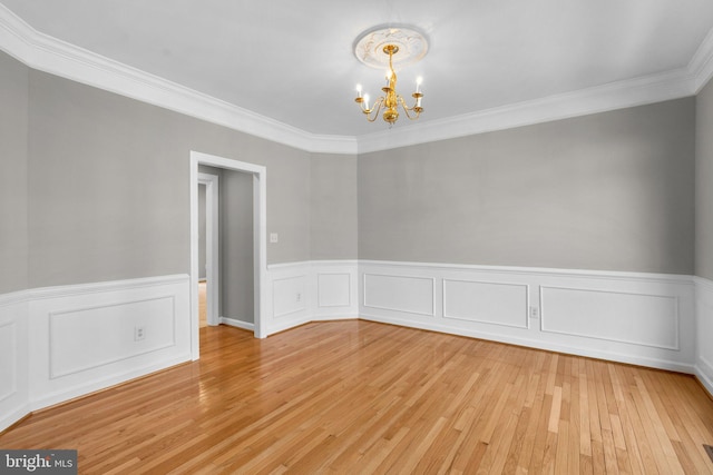 unfurnished room featuring an inviting chandelier, crown molding, light wood-type flooring, and wainscoting