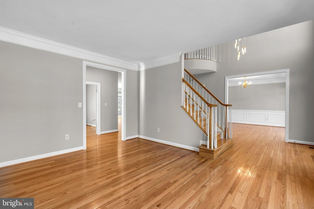 unfurnished living room with stairway, baseboards, light wood-style floors, crown molding, and a chandelier