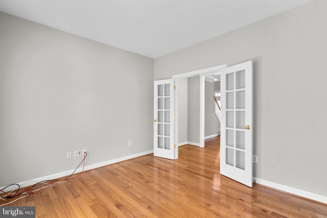 spare room featuring french doors, baseboards, and light wood finished floors