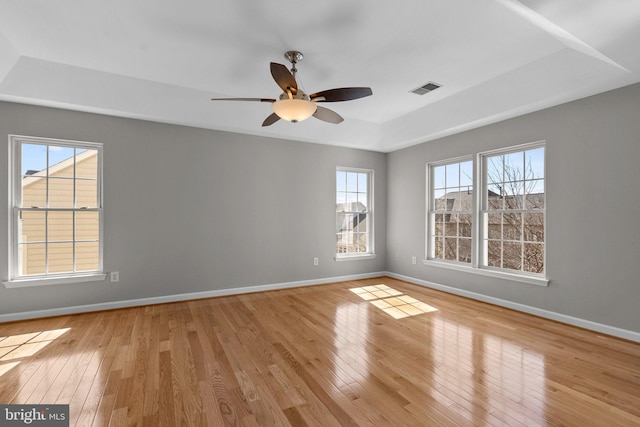 spare room featuring visible vents, a raised ceiling, a ceiling fan, light wood finished floors, and baseboards