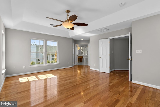 empty room featuring a raised ceiling, light wood-style floors, visible vents, and baseboards