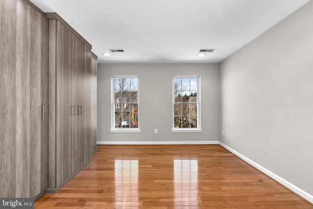 empty room featuring light wood-type flooring, visible vents, and baseboards