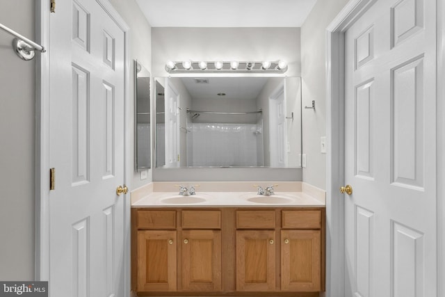 full bathroom with double vanity, walk in shower, and a sink