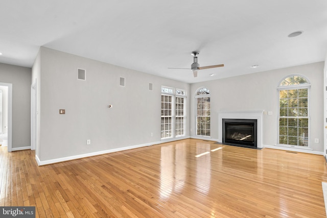 unfurnished living room featuring a fireplace with flush hearth, baseboards, and light wood finished floors