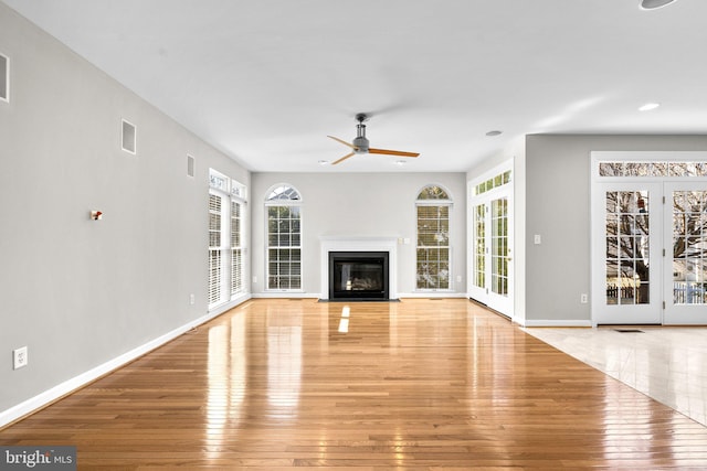 unfurnished living room featuring light wood finished floors, a fireplace with flush hearth, baseboards, and a ceiling fan