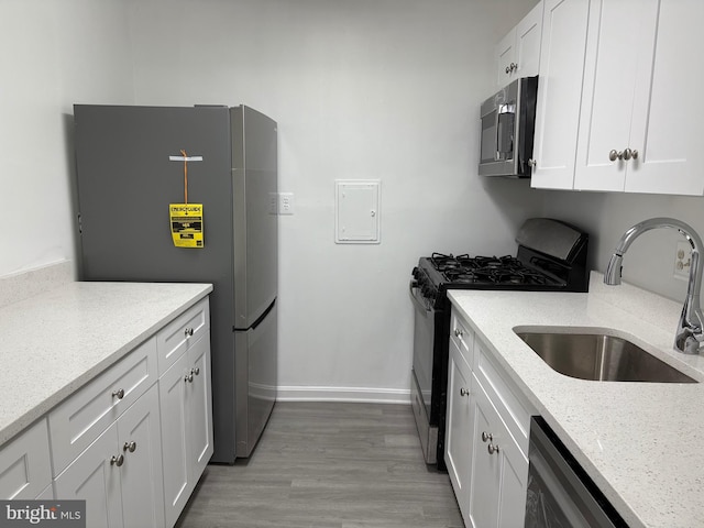 kitchen featuring light stone counters, wood finished floors, a sink, appliances with stainless steel finishes, and white cabinetry