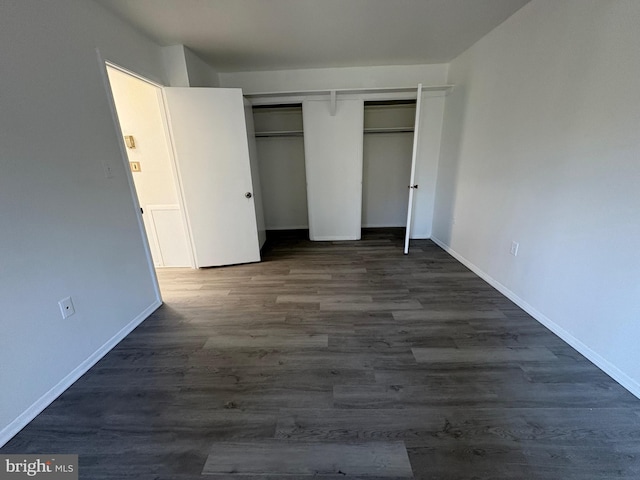 unfurnished bedroom with a closet, baseboards, and dark wood finished floors