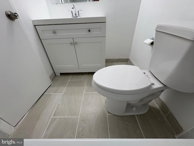 half bath with baseboards, toilet, and vanity