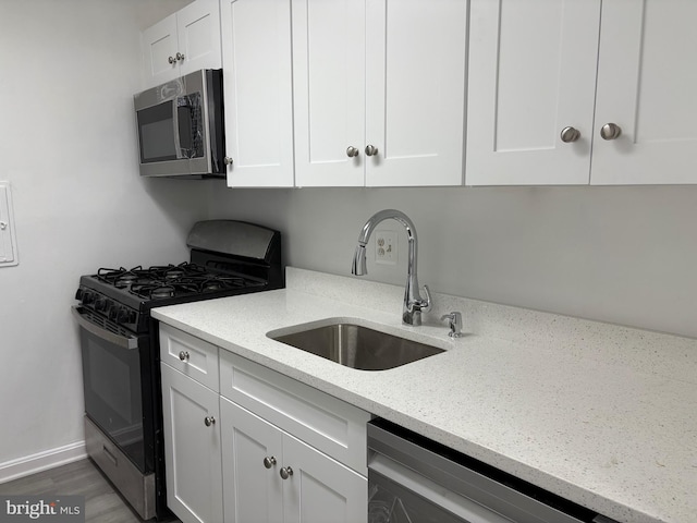 kitchen featuring light stone counters, white cabinets, appliances with stainless steel finishes, and a sink