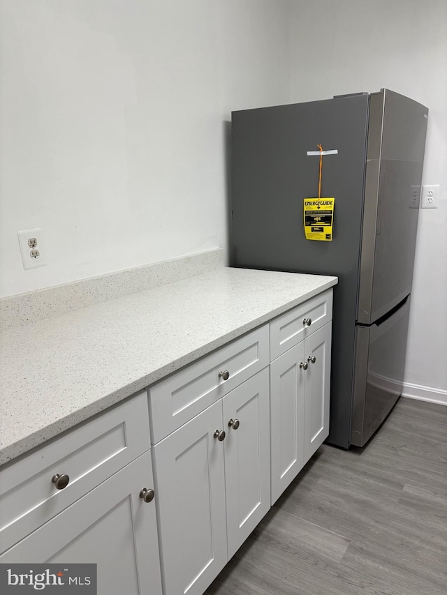 room details with light stone counters, white cabinetry, light wood-style flooring, and freestanding refrigerator