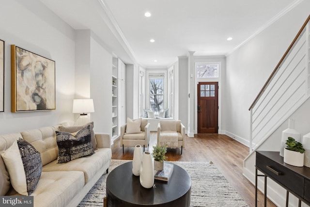 living room with built in features, ornamental molding, and light hardwood / wood-style floors