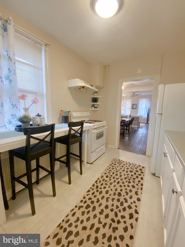 kitchen featuring white appliances, ceiling fan, light tile patterned floors, range hood, and white cabinetry