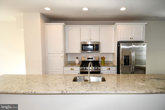 kitchen featuring sink, backsplash, stainless steel appliances, light stone countertops, and white cabinets