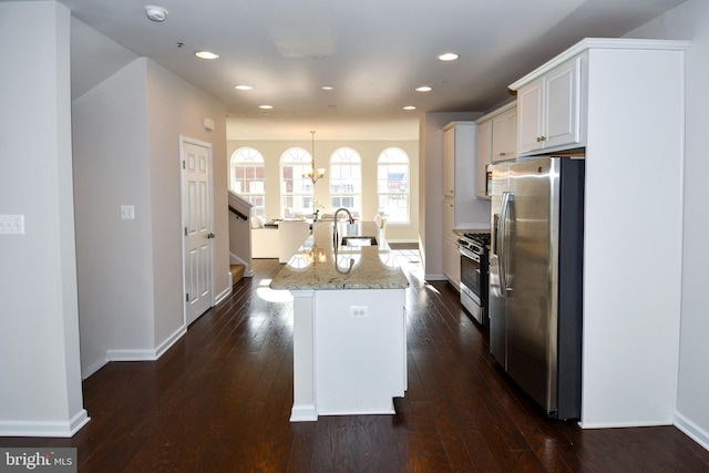 kitchen featuring pendant lighting, white cabinetry, stainless steel appliances, light stone countertops, and an island with sink