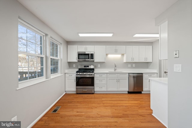 kitchen featuring stainless steel appliances, a healthy amount of sunlight, sink, light hardwood / wood-style flooring, and white cabinetry