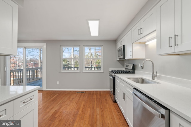 kitchen with sink, white cabinets, light hardwood / wood-style flooring, and appliances with stainless steel finishes