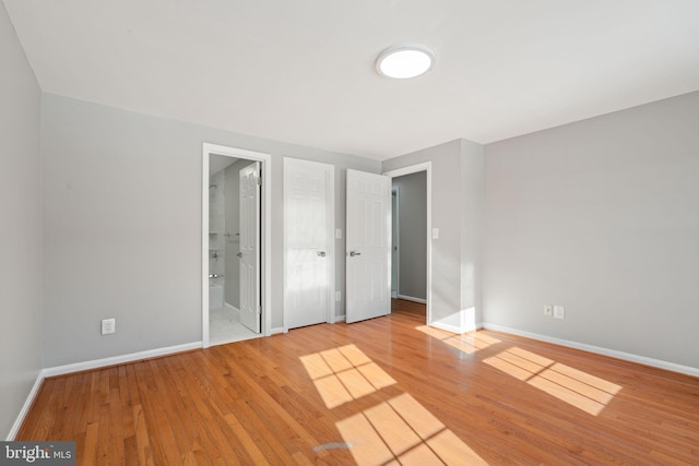 unfurnished bedroom with ensuite bathroom and wood-type flooring