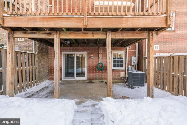 snow covered patio featuring central air condition unit and a deck