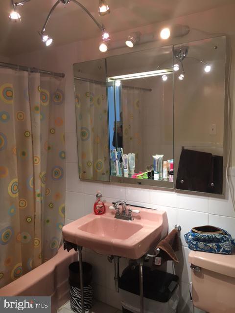 full bathroom featuring backsplash, sink, toilet, tile walls, and shower / tub combo