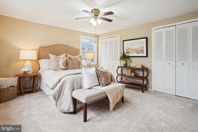 bedroom with multiple closets, light colored carpet, and a ceiling fan