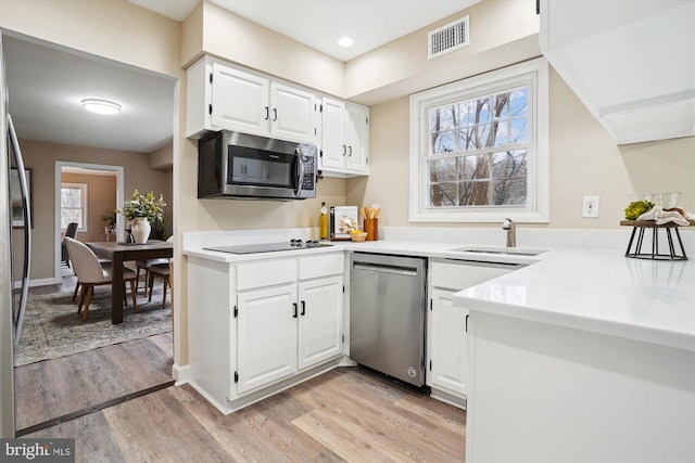 kitchen featuring visible vents, appliances with stainless steel finishes, light wood-style floors, white cabinetry, and a sink