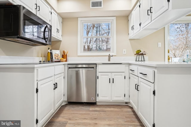 kitchen featuring appliances with stainless steel finishes, visible vents, light wood-style floors, and white cabinetry