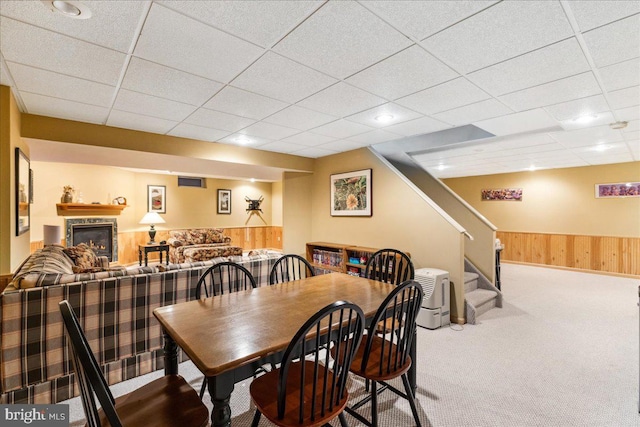 carpeted dining room featuring a drop ceiling and wooden walls