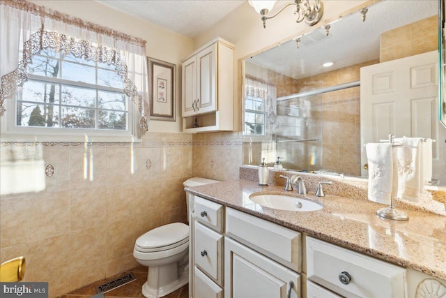 bathroom with tile walls, vanity, a wealth of natural light, and a shower with door