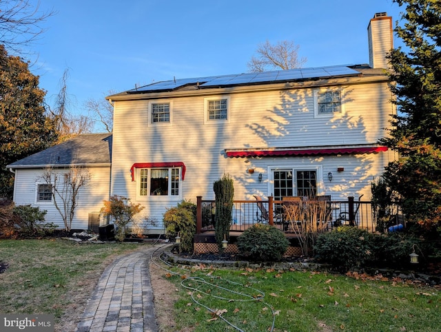 back of property with a wooden deck, a yard, and solar panels