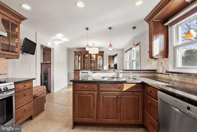 kitchen featuring dark stone counters, glass insert cabinets, decorative light fixtures, a peninsula, and stainless steel appliances