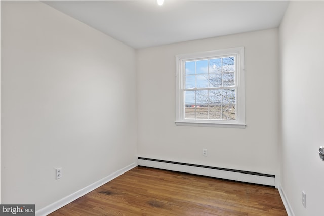 empty room with a baseboard heating unit, baseboards, and wood finished floors