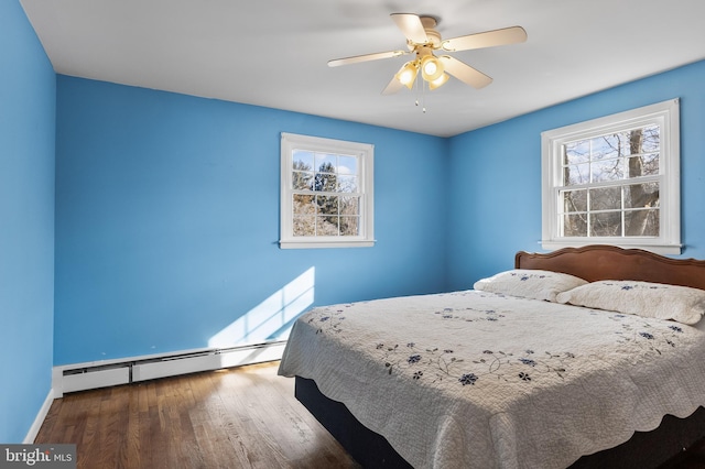 bedroom featuring ceiling fan, multiple windows, baseboard heating, and wood finished floors