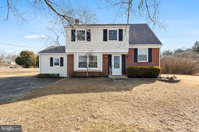 view of front facade with a front yard, brick siding, and a chimney