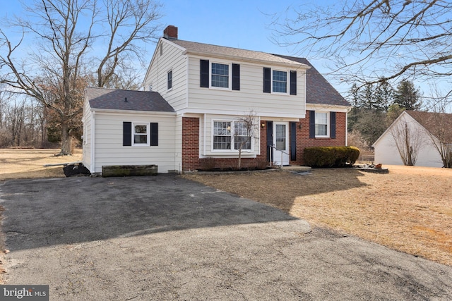 view of front of house featuring driveway, brick siding, a chimney, and a shingled roof