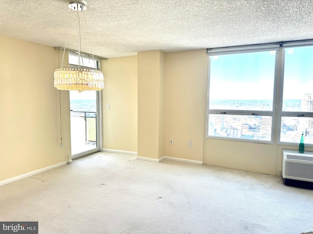 carpeted spare room with a wall mounted air conditioner, a healthy amount of sunlight, a textured ceiling, and an inviting chandelier