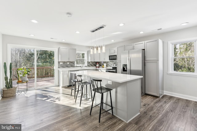 kitchen with appliances with stainless steel finishes, a center island, dark hardwood / wood-style flooring, a breakfast bar, and pendant lighting