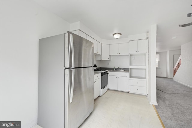 kitchen featuring stainless steel refrigerator, white gas stove, sink, light carpet, and white cabinets