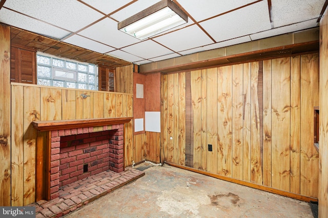 living room featuring a fireplace, concrete floors, a drop ceiling, and wooden walls