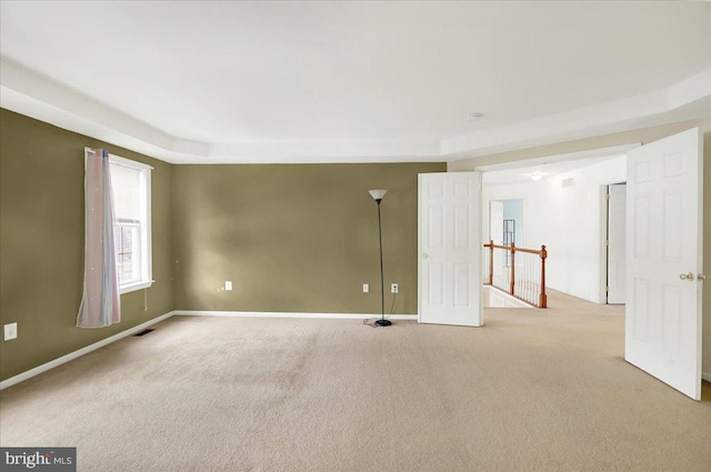 empty room featuring a tray ceiling and light colored carpet