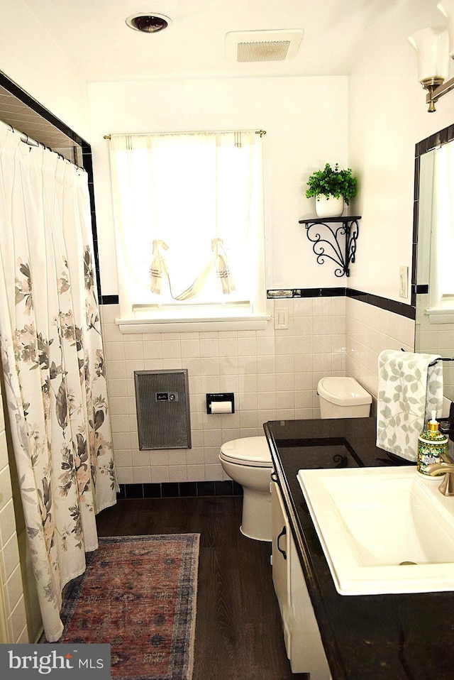 bathroom with hardwood / wood-style floors, vanity, toilet, tile walls, and heating unit