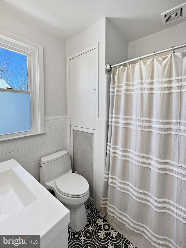 bathroom featuring vanity, toilet, and tile walls