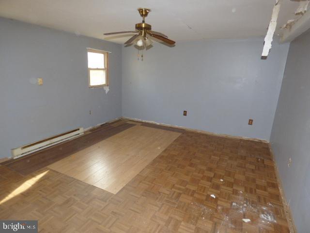 unfurnished room with ceiling fan, parquet floors, and a baseboard heating unit