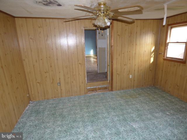 carpeted empty room featuring ceiling fan and wood walls