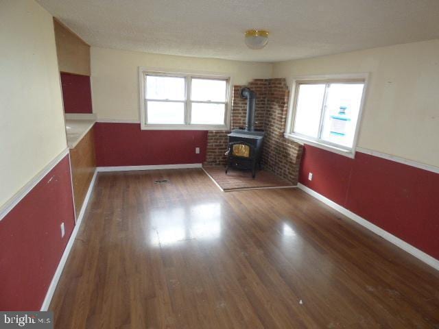 unfurnished living room with a wood stove, dark hardwood / wood-style flooring, a healthy amount of sunlight, and brick wall