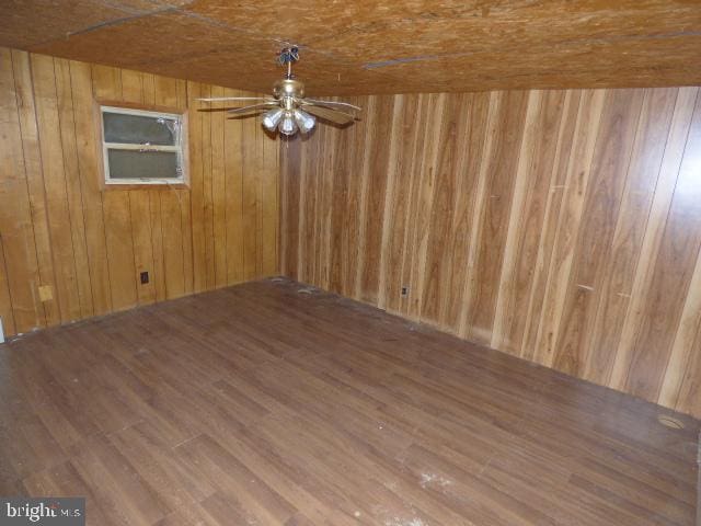 empty room featuring hardwood / wood-style flooring, ceiling fan, and wood walls