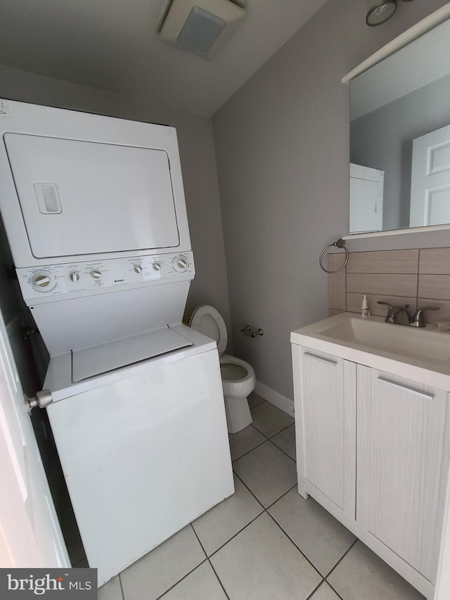 bathroom featuring decorative backsplash, tile patterned floors, vanity, toilet, and stacked washer / drying machine