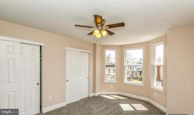 unfurnished bedroom featuring multiple closets, ceiling fan, and carpet floors