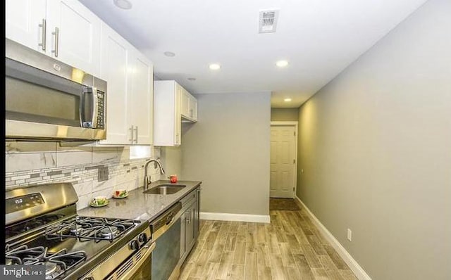 kitchen featuring dark stone counters, white cabinets, sink, light wood-type flooring, and stainless steel appliances