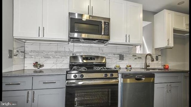 kitchen with dark stone counters, white cabinets, sink, tasteful backsplash, and stainless steel appliances