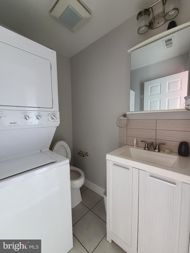 bathroom featuring decorative backsplash, tile patterned floors, vanity, stacked washer / dryer, and toilet